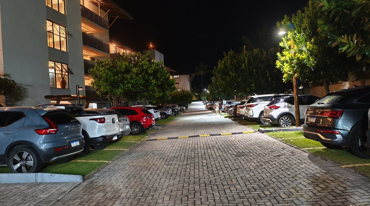 Estacionamento interno do condomínio à noite, iluminado, com vagas em frente aos blocos